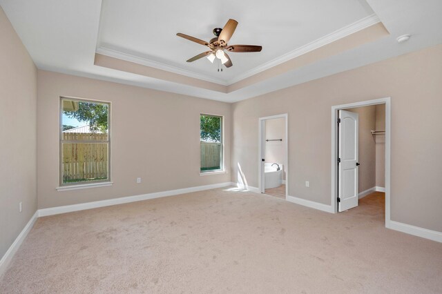 unfurnished bedroom featuring a raised ceiling, ceiling fan, a spacious closet, and ensuite bathroom