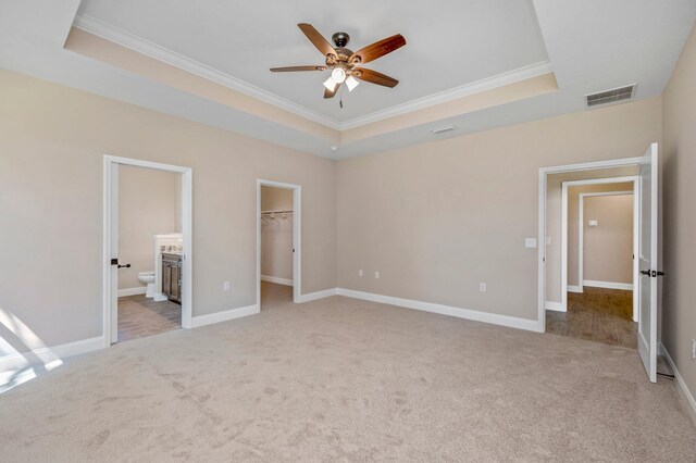 unfurnished bedroom with ceiling fan, a raised ceiling, a spacious closet, and ensuite bath