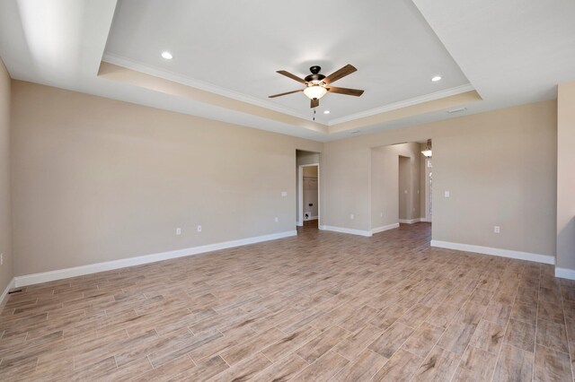 spare room with a tray ceiling, light wood-type flooring, ornamental molding, and ceiling fan