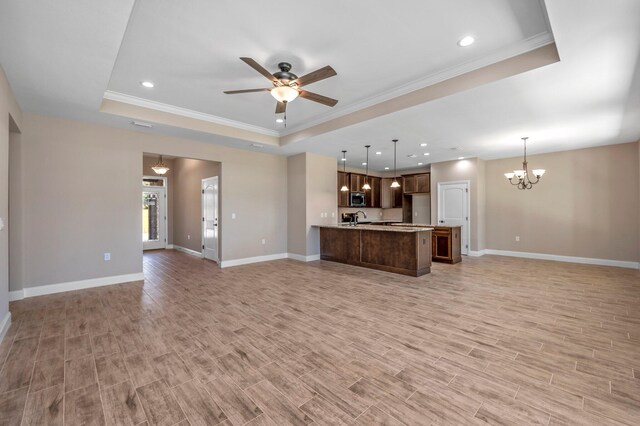 unfurnished living room featuring ceiling fan with notable chandelier, light wood-type flooring, and a tray ceiling