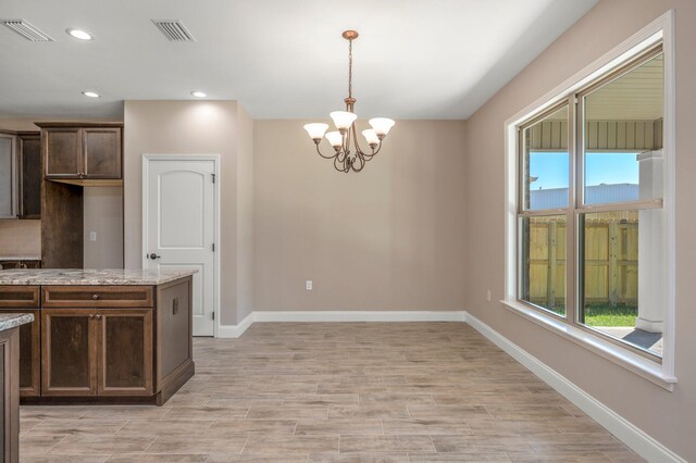 kitchen featuring light wood-type flooring, a notable chandelier, decorative light fixtures, light stone countertops, and dark brown cabinetry