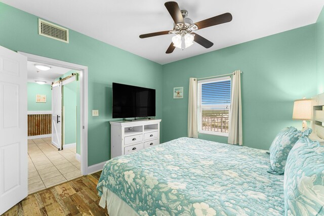 bedroom featuring a barn door, ceiling fan, and hardwood / wood-style flooring