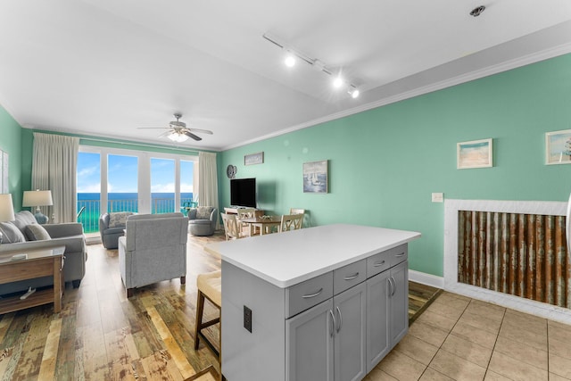 kitchen featuring light hardwood / wood-style flooring, gray cabinets, ceiling fan, a kitchen island, and ornamental molding