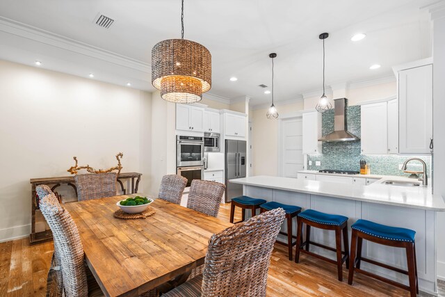 dining area featuring crown molding, sink, and light hardwood / wood-style flooring