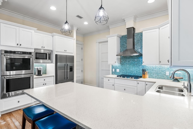 kitchen featuring wall chimney range hood, stainless steel appliances, and white cabinets