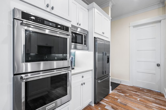 kitchen with ornamental molding, white cabinets, appliances with stainless steel finishes, and light wood-type flooring