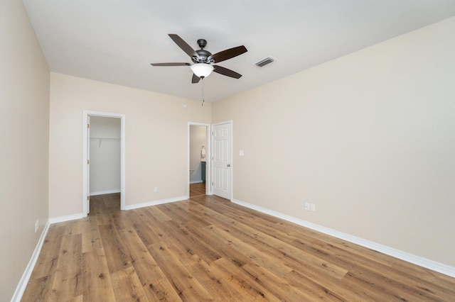 unfurnished bedroom with a spacious closet, ceiling fan, a closet, and light hardwood / wood-style flooring