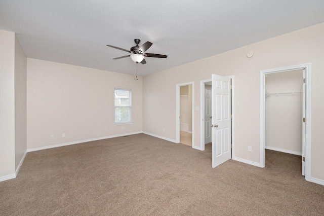 unfurnished bedroom featuring ceiling fan, a closet, light carpet, and a walk in closet