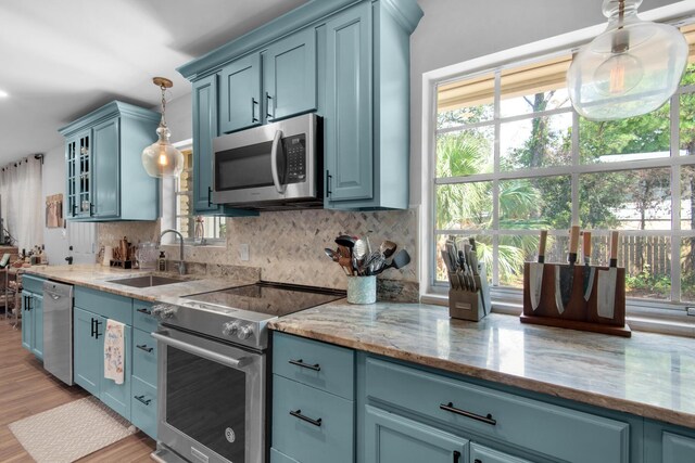 kitchen with backsplash, light hardwood / wood-style flooring, decorative light fixtures, appliances with stainless steel finishes, and sink