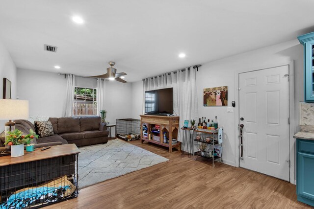 living room featuring ceiling fan, light wood-type flooring, and a fireplace