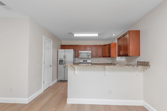 kitchen with kitchen peninsula, a kitchen breakfast bar, appliances with stainless steel finishes, and light hardwood / wood-style floors