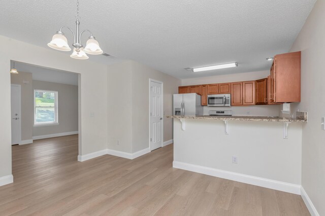 kitchen featuring hanging light fixtures, light hardwood / wood-style flooring, stainless steel appliances, a notable chandelier, and kitchen peninsula