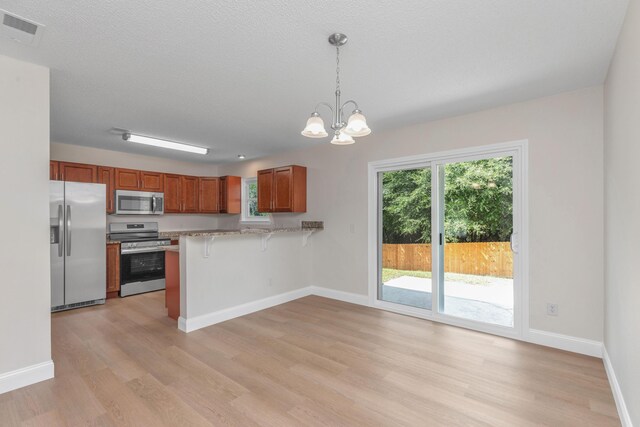 kitchen with hanging light fixtures, appliances with stainless steel finishes, a chandelier, kitchen peninsula, and a breakfast bar area