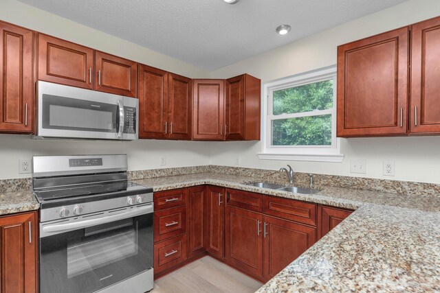 kitchen featuring a textured ceiling, stainless steel appliances, light stone counters, sink, and light hardwood / wood-style floors