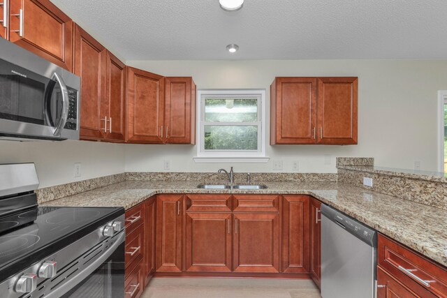 kitchen with a textured ceiling, light stone counters, stainless steel appliances, and sink