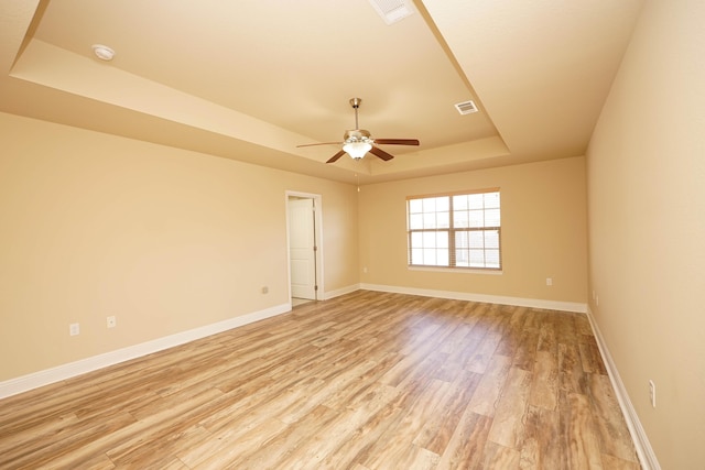 unfurnished room featuring ceiling fan, light hardwood / wood-style floors, and a tray ceiling