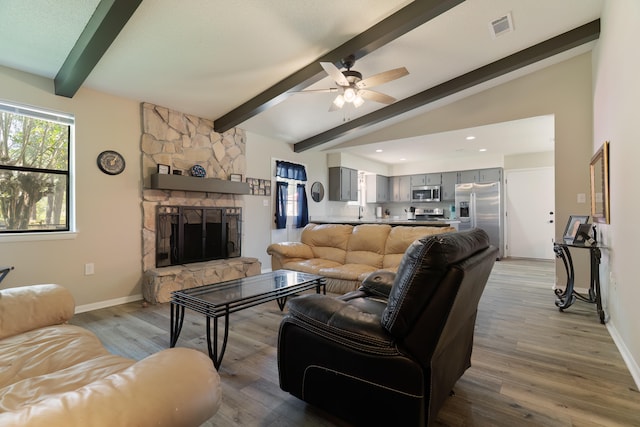 living room featuring ceiling fan, lofted ceiling with beams, a stone fireplace, and light hardwood / wood-style flooring