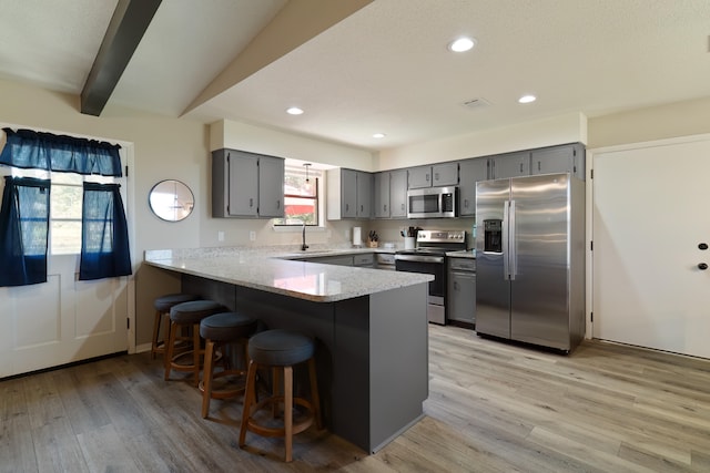 kitchen with kitchen peninsula, appliances with stainless steel finishes, gray cabinetry, light hardwood / wood-style floors, and a breakfast bar area