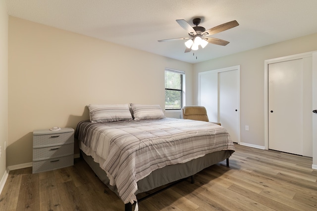 bedroom featuring a textured ceiling, light hardwood / wood-style floors, ceiling fan, and multiple closets