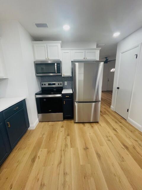 kitchen featuring backsplash, white cabinetry, stainless steel appliances, and light hardwood / wood-style floors