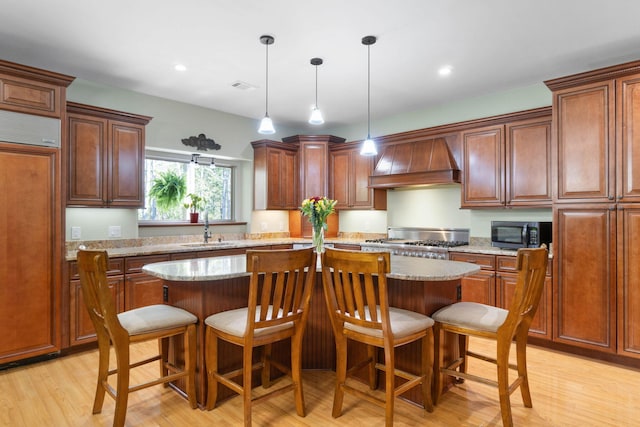 kitchen featuring light stone counters, custom exhaust hood, a kitchen island, paneled fridge, and light wood-type flooring