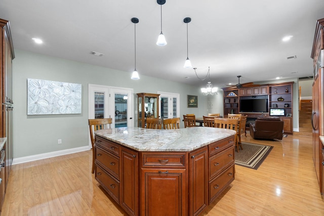 kitchen with light hardwood / wood-style floors, a center island, ceiling fan with notable chandelier, decorative light fixtures, and light stone countertops