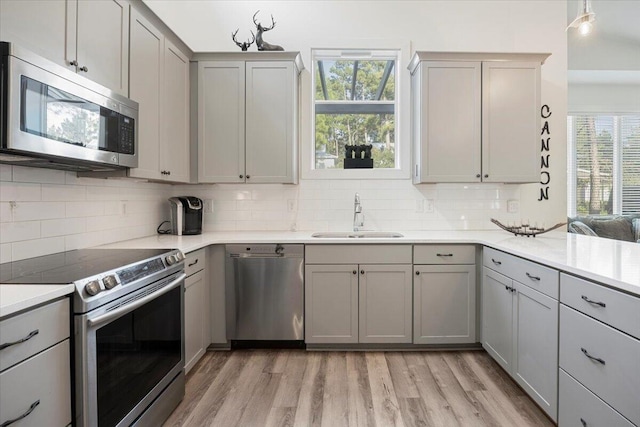 kitchen with light wood-type flooring, gray cabinetry, stainless steel appliances, and sink