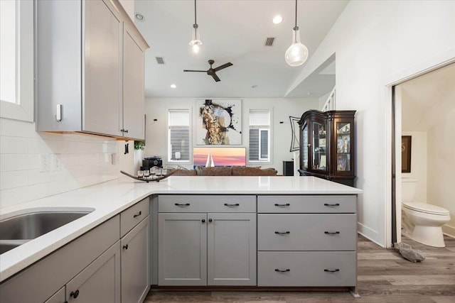 kitchen featuring gray cabinetry, hanging light fixtures, light hardwood / wood-style floors, kitchen peninsula, and tasteful backsplash