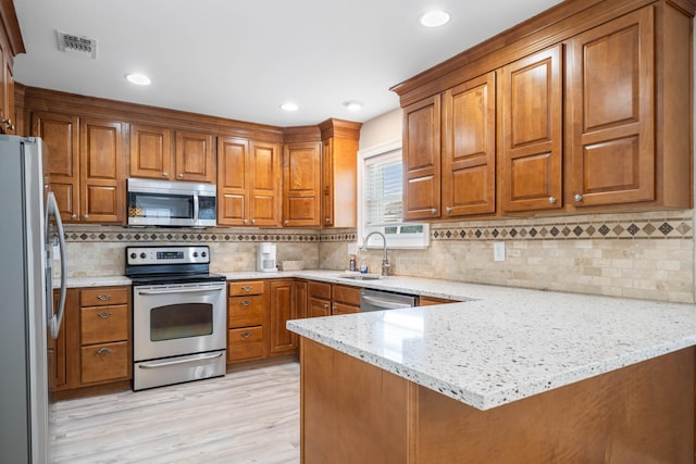 kitchen with light stone counters, kitchen peninsula, stainless steel appliances, and light hardwood / wood-style floors