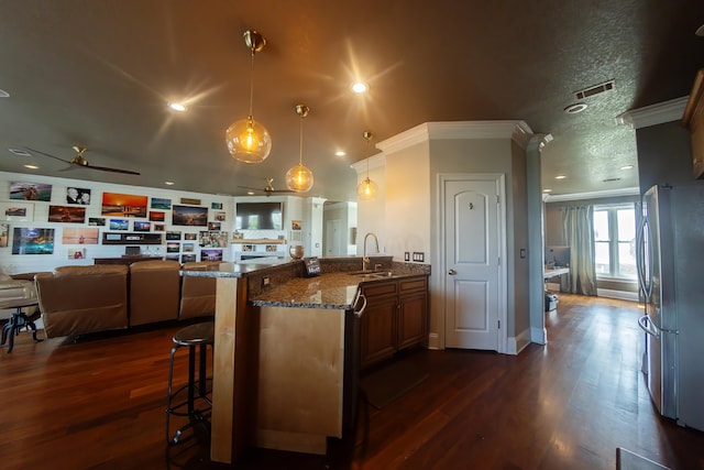 kitchen with ceiling fan, pendant lighting, stainless steel refrigerator, a kitchen breakfast bar, and dark hardwood / wood-style flooring