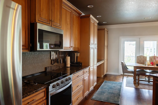 kitchen with dark stone countertops, ornamental molding, appliances with stainless steel finishes, and dark wood-type flooring