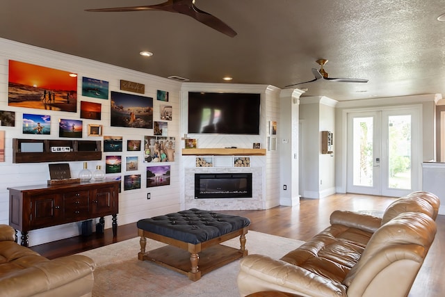 living room with light wood-type flooring, a textured ceiling, a fireplace, crown molding, and ceiling fan