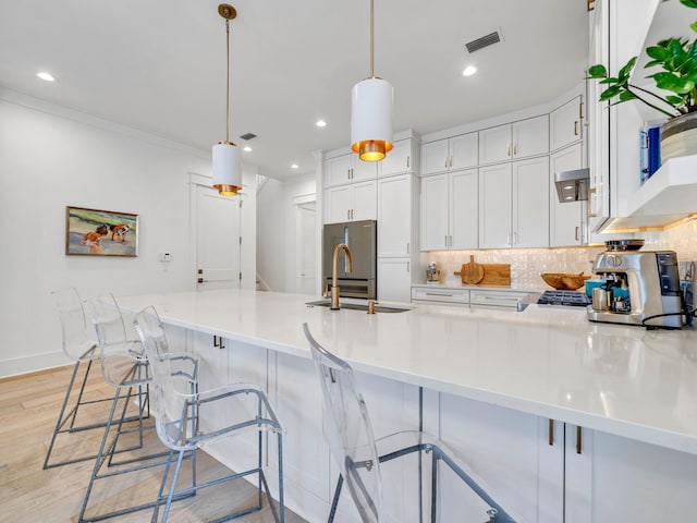 kitchen featuring pendant lighting, backsplash, sink, light hardwood / wood-style flooring, and white cabinetry