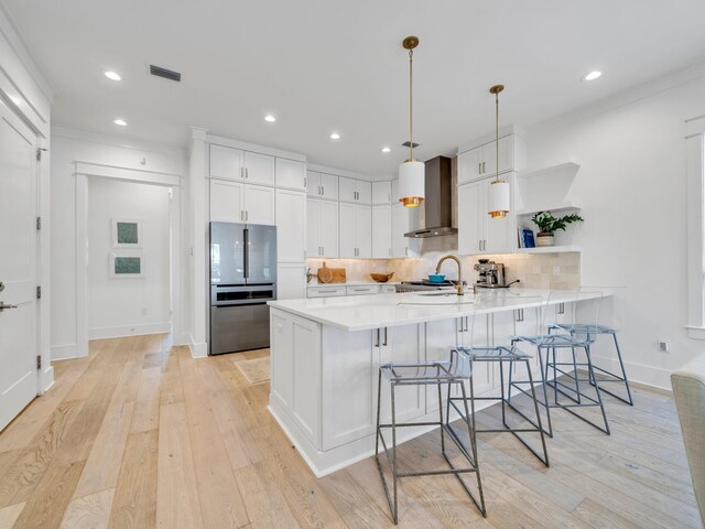 kitchen featuring a kitchen bar, kitchen peninsula, wall chimney exhaust hood, pendant lighting, and white cabinets