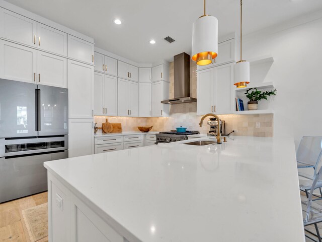 kitchen featuring white cabinets, sink, wall chimney exhaust hood, decorative light fixtures, and stainless steel appliances