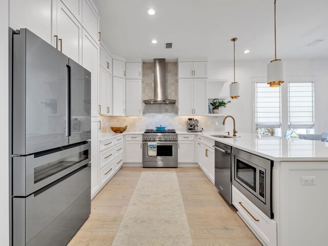 kitchen with wall chimney range hood, tasteful backsplash, decorative light fixtures, white cabinets, and appliances with stainless steel finishes