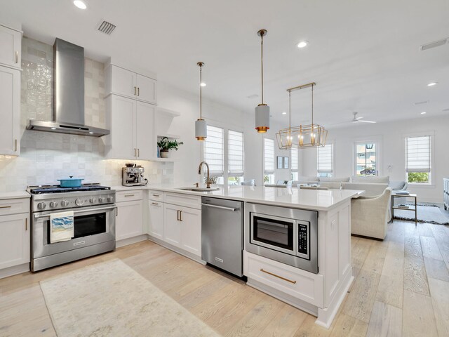 kitchen featuring wall chimney exhaust hood, stainless steel appliances, ceiling fan, white cabinetry, and hanging light fixtures