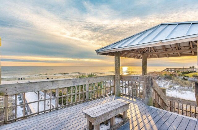 deck at dusk featuring a gazebo, a water view, and a beach view