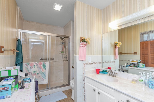 bathroom with tile walls, a textured ceiling, a shower with door, vanity, and toilet