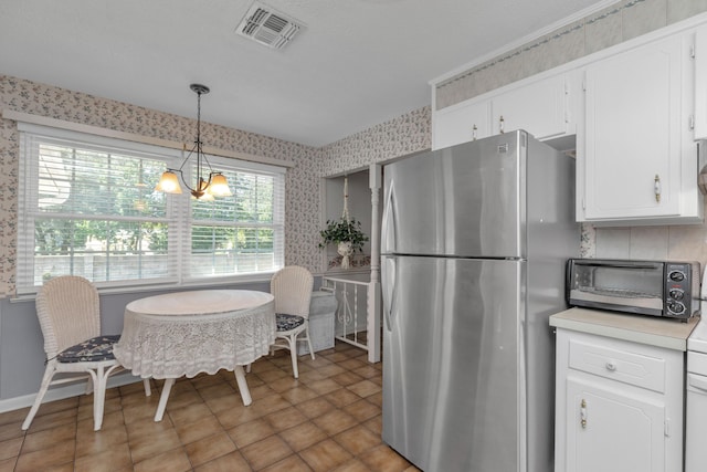 kitchen featuring stainless steel fridge, white cabinetry, pendant lighting, and a notable chandelier