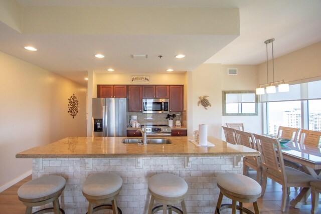 kitchen with hanging light fixtures, light stone counters, stainless steel appliances, a kitchen bar, and sink