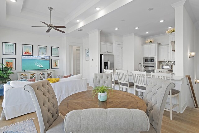 dining room featuring a raised ceiling, light wood-type flooring, ceiling fan, ornamental molding, and sink