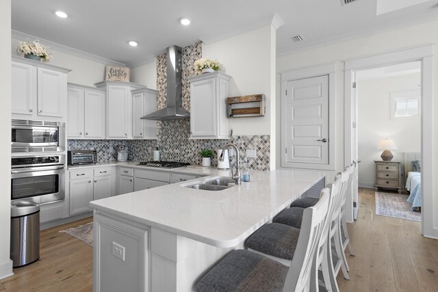 kitchen featuring appliances with stainless steel finishes, a breakfast bar, kitchen peninsula, sink, and wall chimney range hood