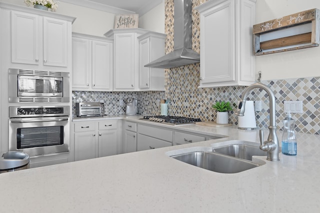 kitchen with appliances with stainless steel finishes, white cabinets, backsplash, sink, and wall chimney range hood