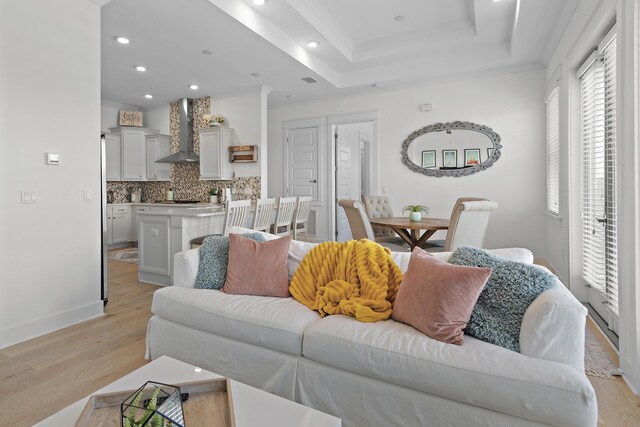 living room with ornamental molding, light hardwood / wood-style flooring, and a raised ceiling