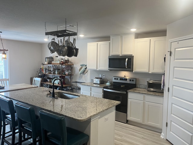 kitchen featuring white cabinets, appliances with stainless steel finishes, a kitchen island with sink, and sink