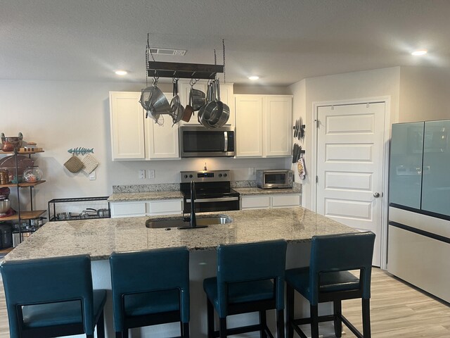 kitchen with light hardwood / wood-style floors, light stone counters, an island with sink, white cabinets, and stainless steel appliances