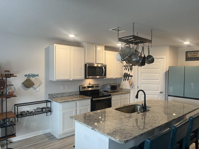 kitchen with an island with sink, white cabinetry, sink, and stainless steel appliances