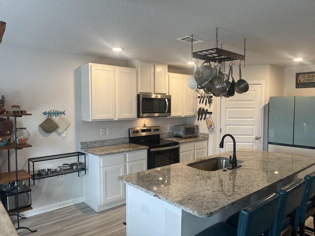 kitchen featuring light stone counters, a kitchen island with sink, sink, white cabinetry, and appliances with stainless steel finishes