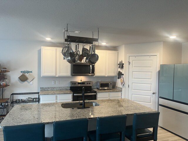 kitchen with light hardwood / wood-style floors, white cabinets, light stone countertops, stainless steel appliances, and a center island with sink